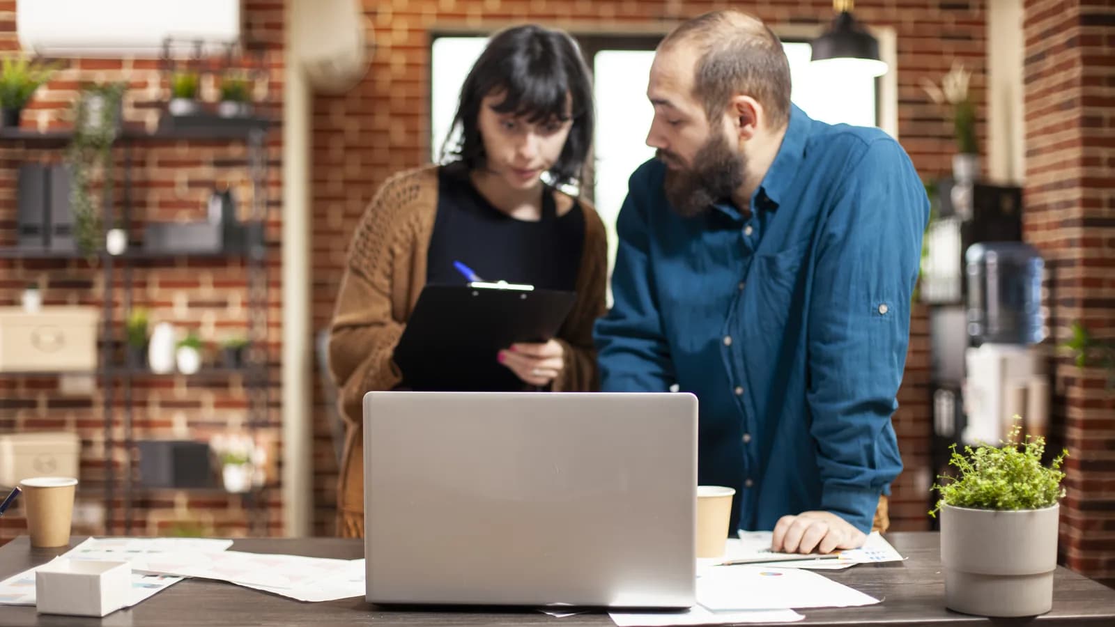 Deux collègues comparent leurs notes devant un ordinateur portable, dans un bureau