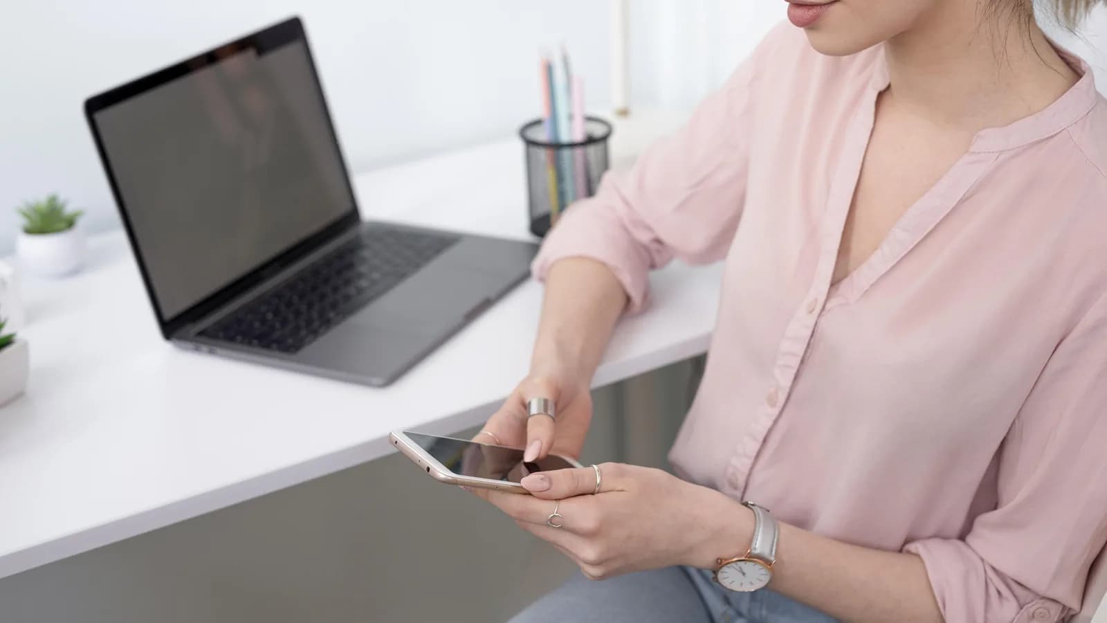 Une femme remplit un formulaire sur son téléphone, assise à son bureau devant un ordinateur portable
