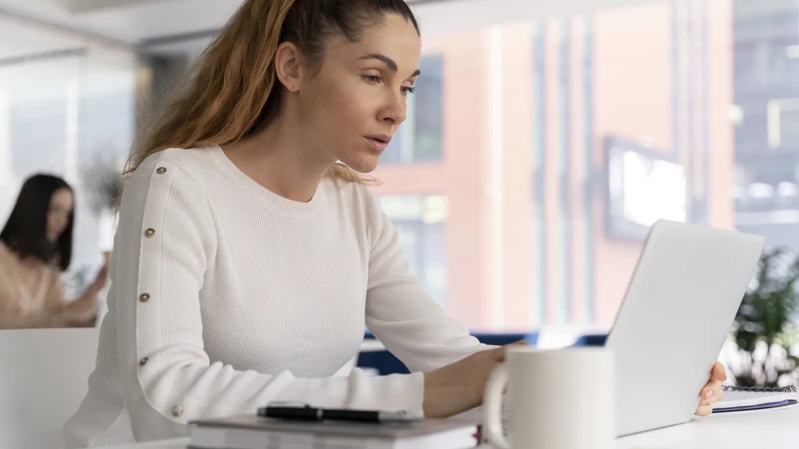 Une femme vérifie sa boîte de réception sur son ordinateur portable, dans un bureau lumineux